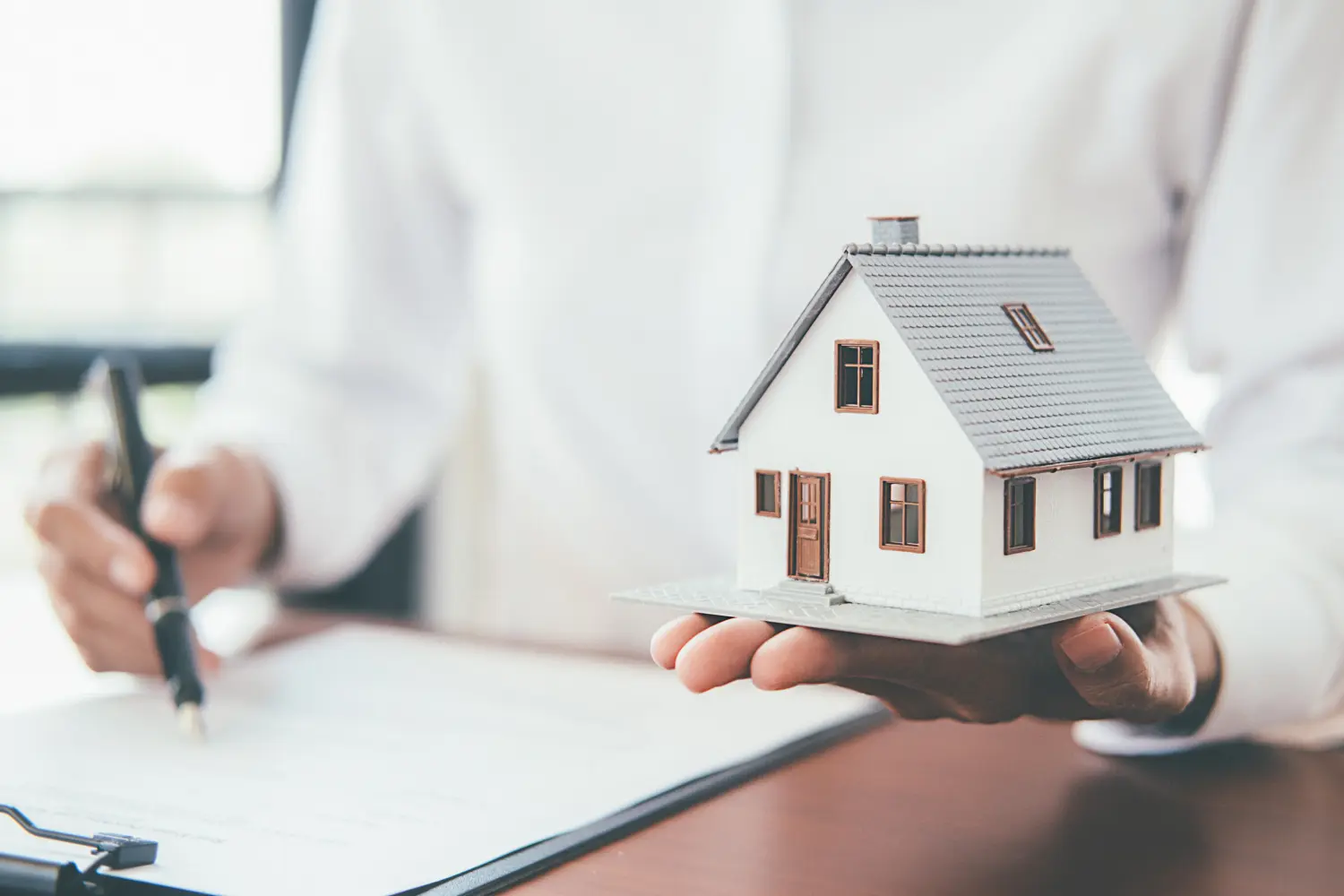 Hausmodell mit Immobilienmakler und Kunde, die einen Vertrag zum Hauskauf, eine Versicherung oder ein Darlehen mit Immobilienhintergrund besprechen.